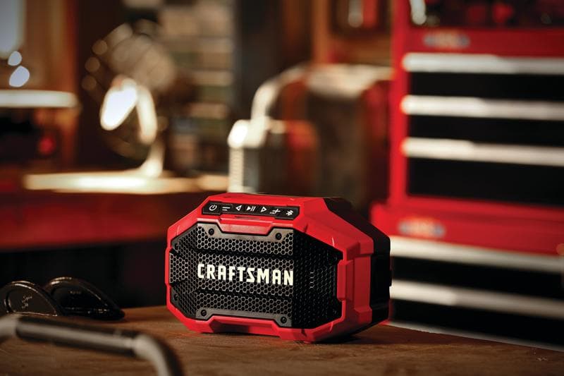 Photo of Craftsman CMCR001B red and black portable Bluetooth speaker on a workbench in a workshop setting.