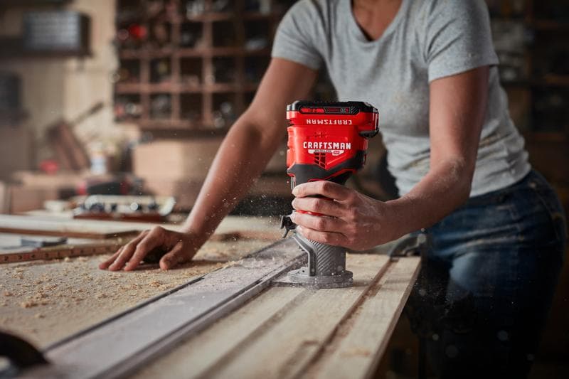 Photo of a person using a Craftsman handheld router, SKU CMCW400B, on a wooden board in a workshop.