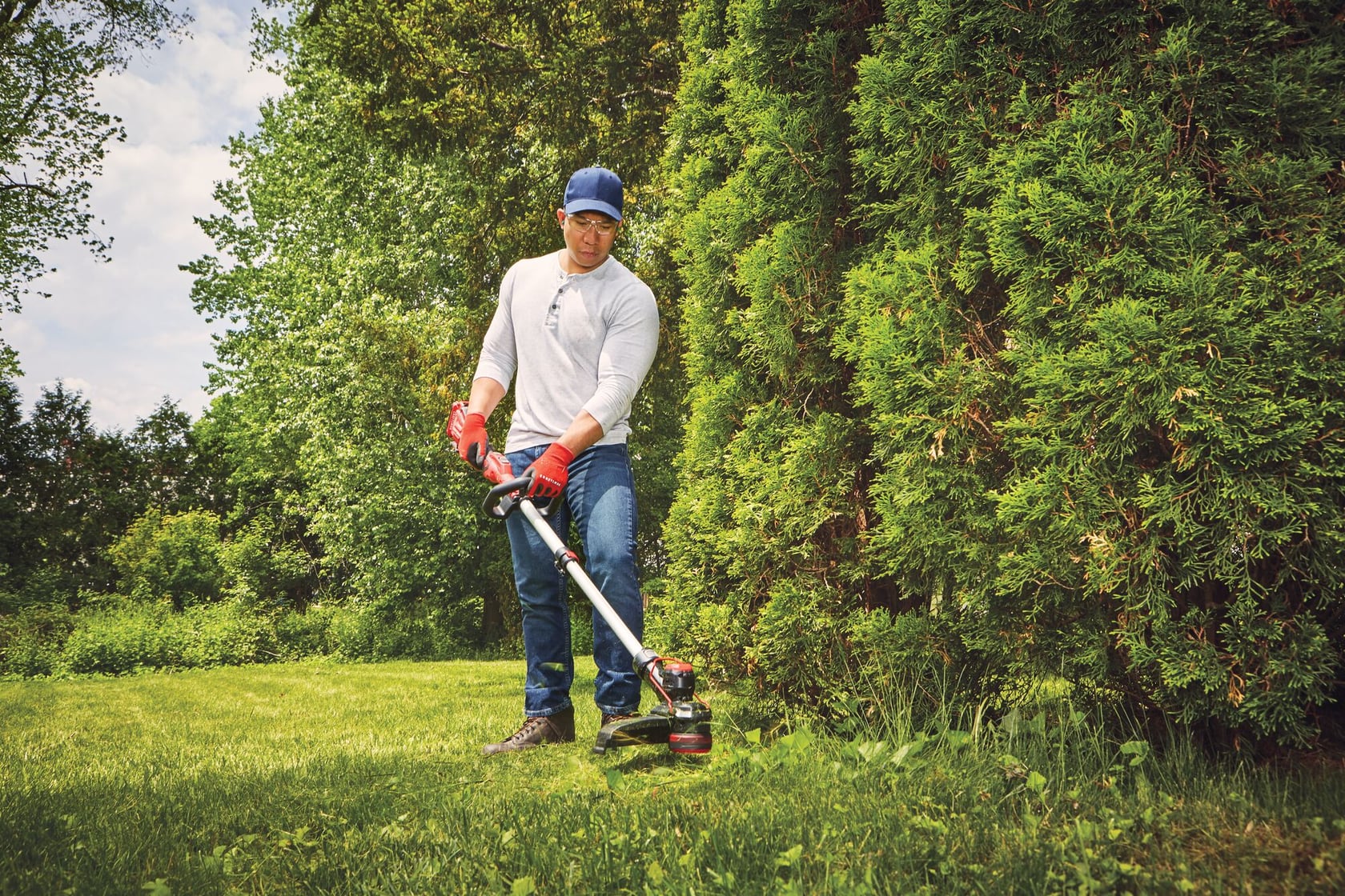 Photo of a person using a Craftsman string trimmer CMCST910B in a yard, trimming grass near bushes.
