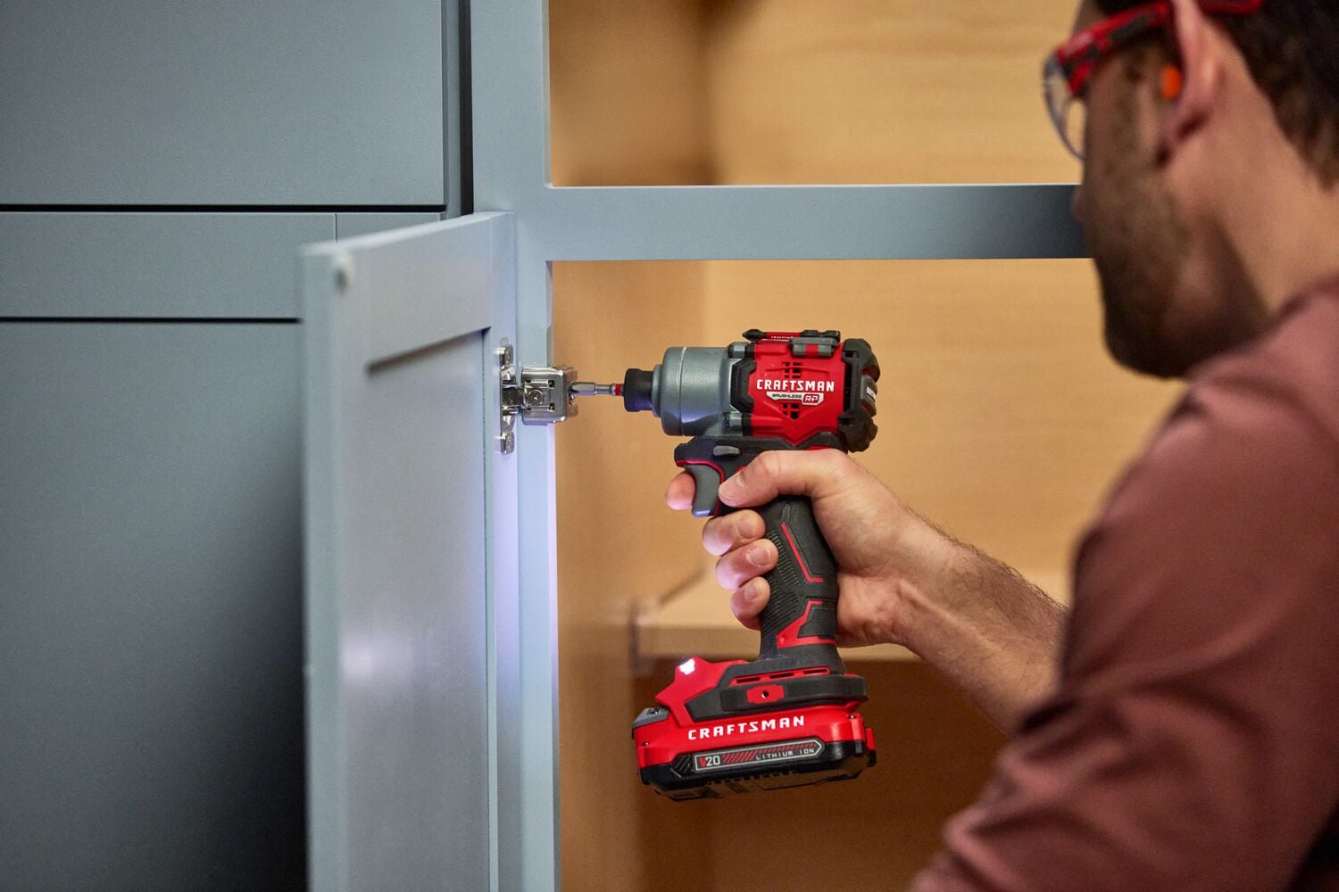 Photo of Craftsman CMCF830D2 impact driver used on cabinet hinge, close-up view of tool in use.