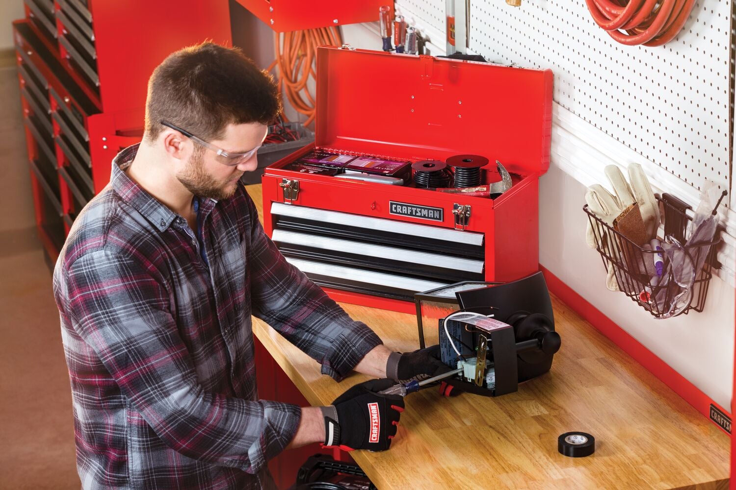 Portable 20 and 5 tenths inch Ball bearing 3 Drawer Red Steel Lockable Tool Box containing tools in use by person working on inner mechanism of a device.