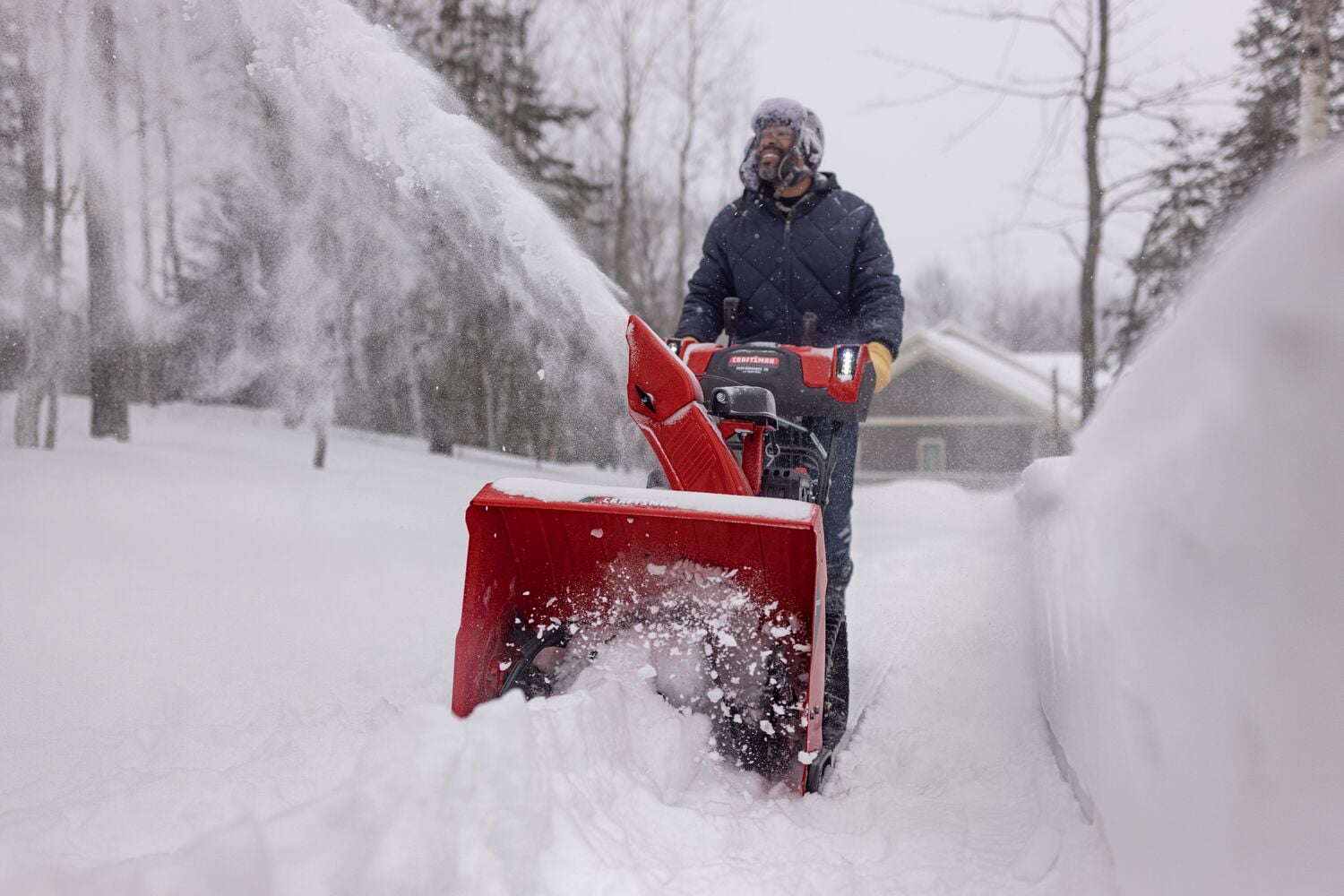 CRAFTSMAN Performance 26 Track Gas Snow Blower clearing snow with trees and house in background