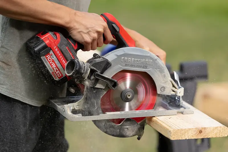 Person using a CRAFTSMAN cordless circular saw to cut a wooden board outdoors.