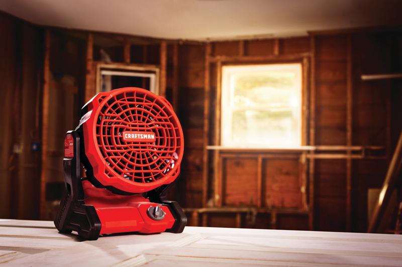Craftsman CMCE001B red and black cordless jobsite fan on a workbench in a construction room.