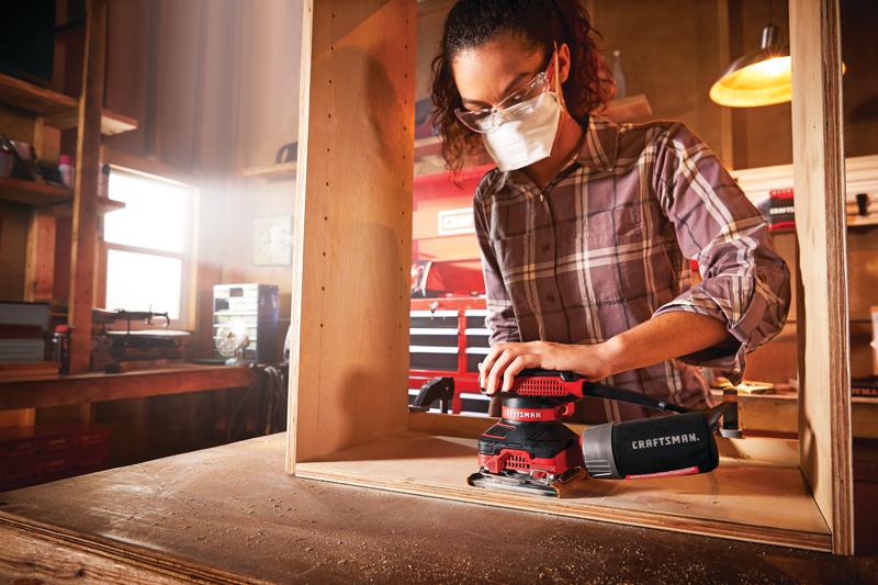Photo of Craftsman CMEW230 sander in use on wood in a workshop, with dust bag attached, visible hands and torso.