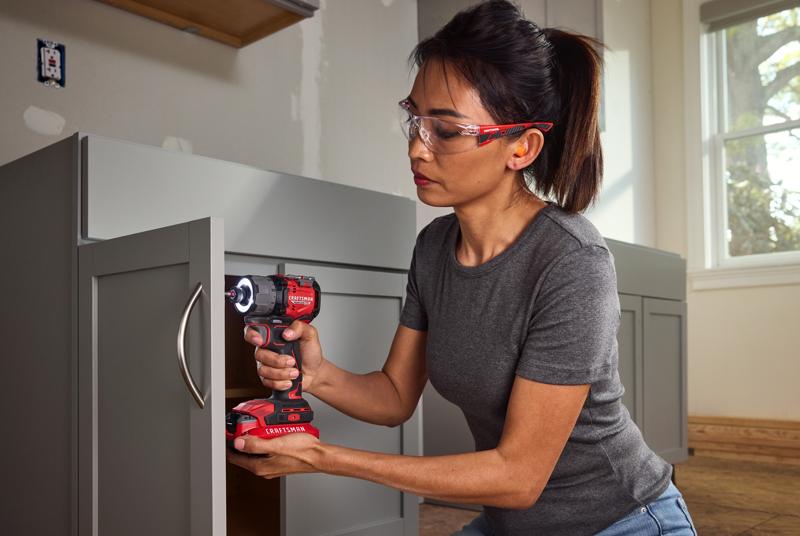 Person using CRAFTSMAN cordless impact driver model CMCF610B to install hardware on gray cabinet, indoor setting.