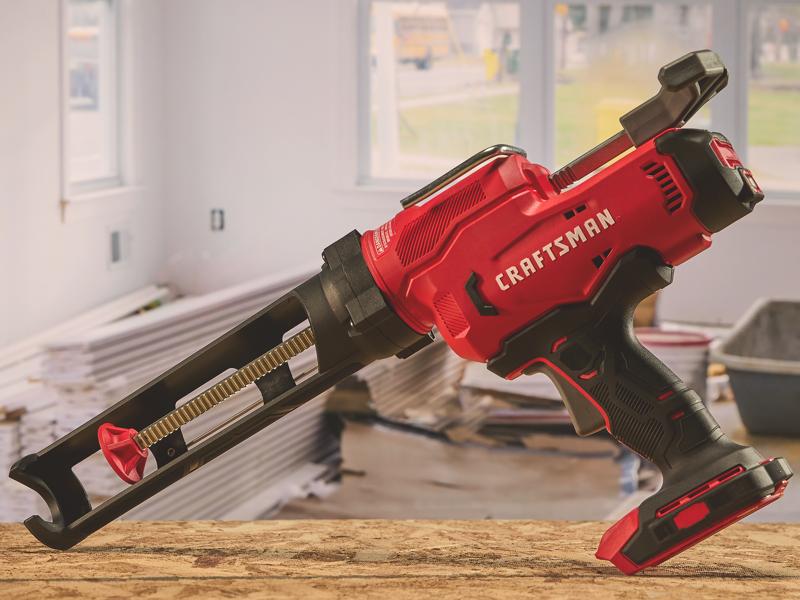 Photo of Craftsman cordless caulk gun, SKU CMCE600, red and black, shown on a table in a workshop setting.