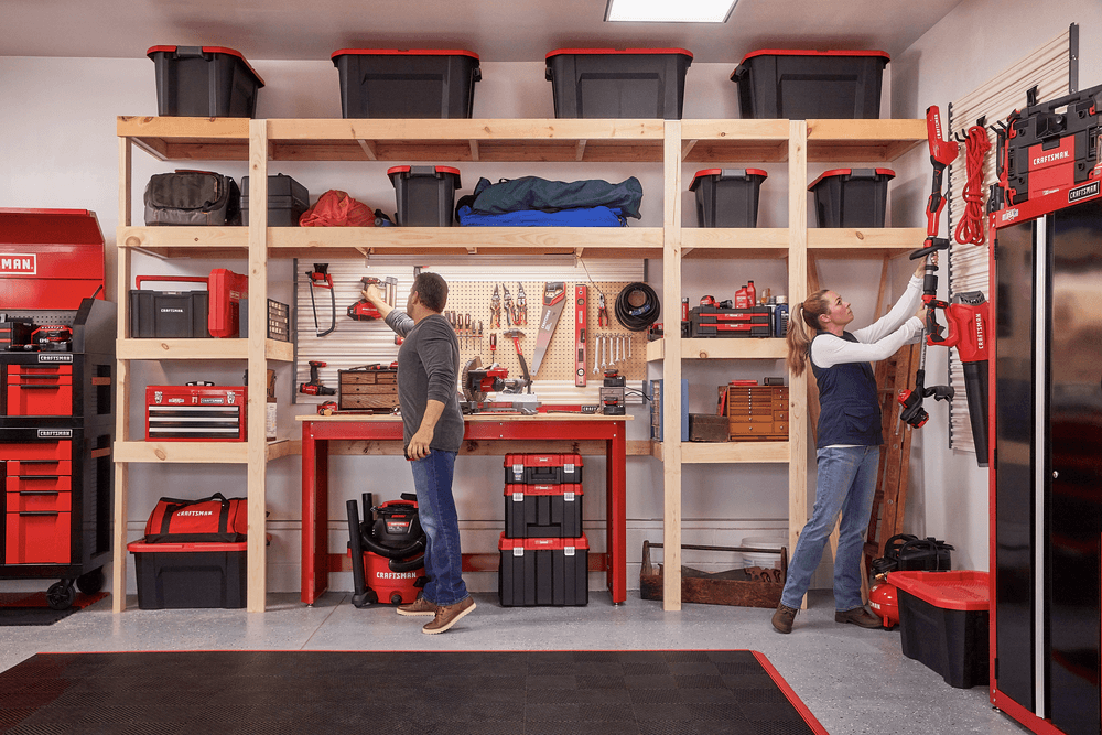 Two persons mounting tools and other lawn equipment on two Versa Track 5 and 5 tenths inch White Composite Multipurpose Storage Rail Systems installed on two different walls of a workshop.