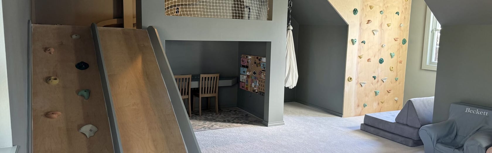 Photo of indoor playroom with slide, climbing wall, study nook with chairs, and gray seating, no visible SKU.