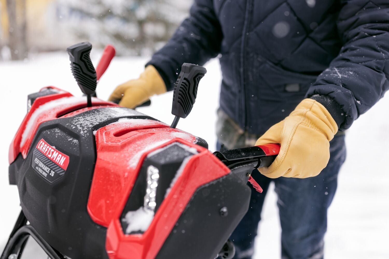 Photo of CRAFTSMAN snow blower CMGB223104 control panel with red and black levers, person wearing gloves operating it.
