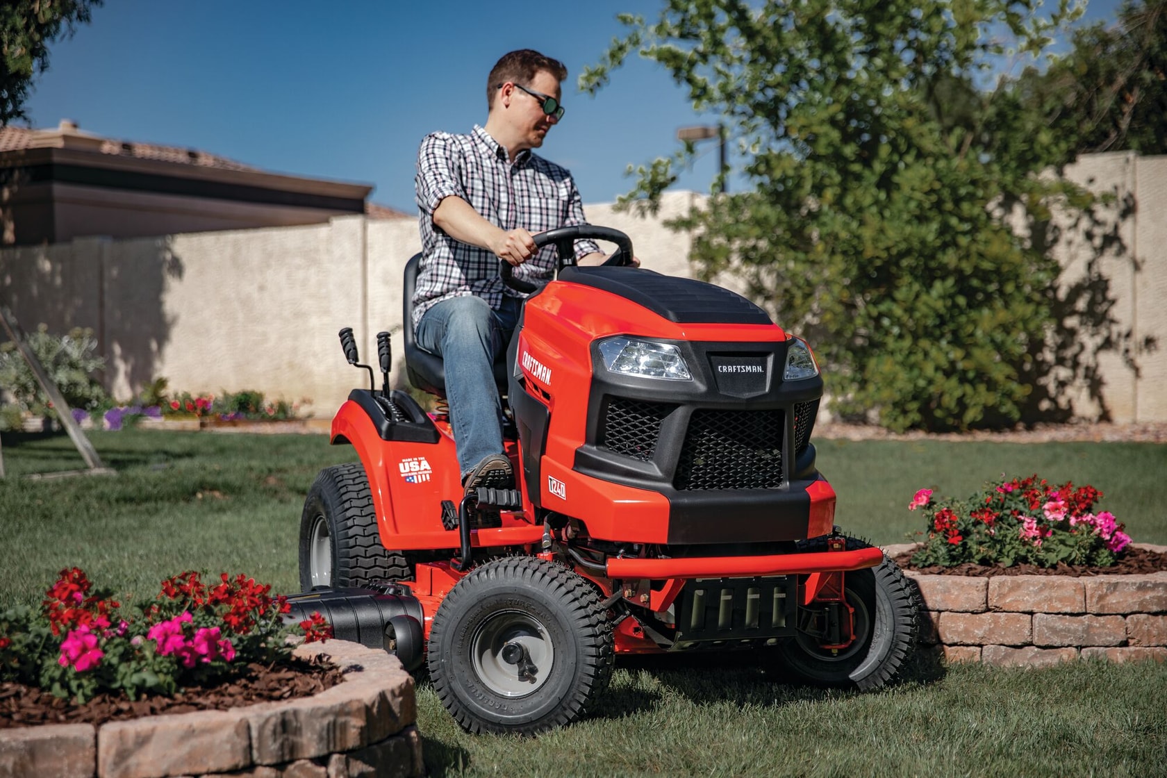 Photo of Craftsman riding lawn mower, SKU CMXGRAM1130044, in use on residential grass lawn near flower beds.