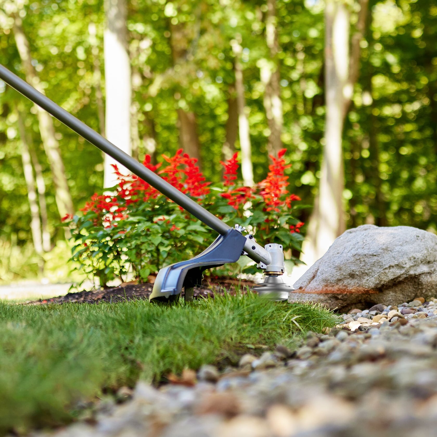 Photo of Craftsman string trimmer 41AJFH-C949 trimming grass near flowers and rocks outdoors.