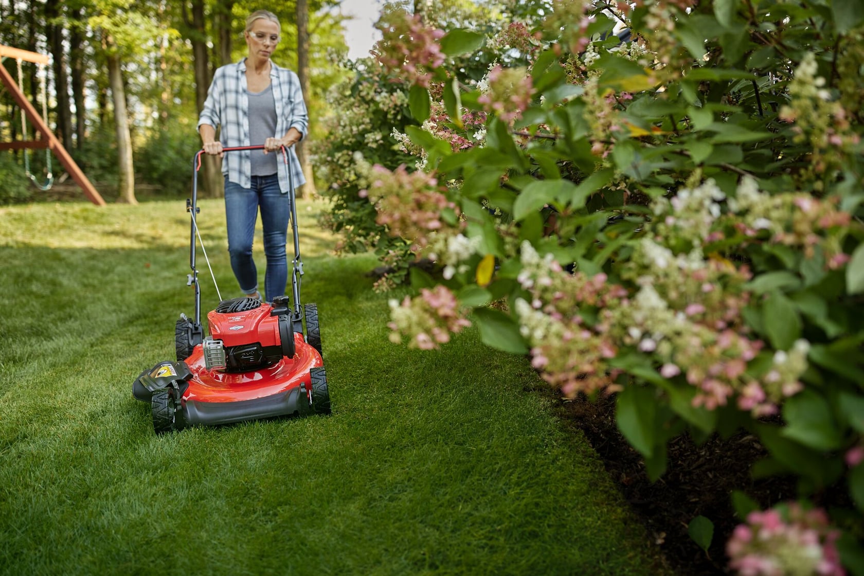 Photo of Craftsman lawn mower SKU CMXGMAM201102 in use on grass near flowering bushes outdoors.