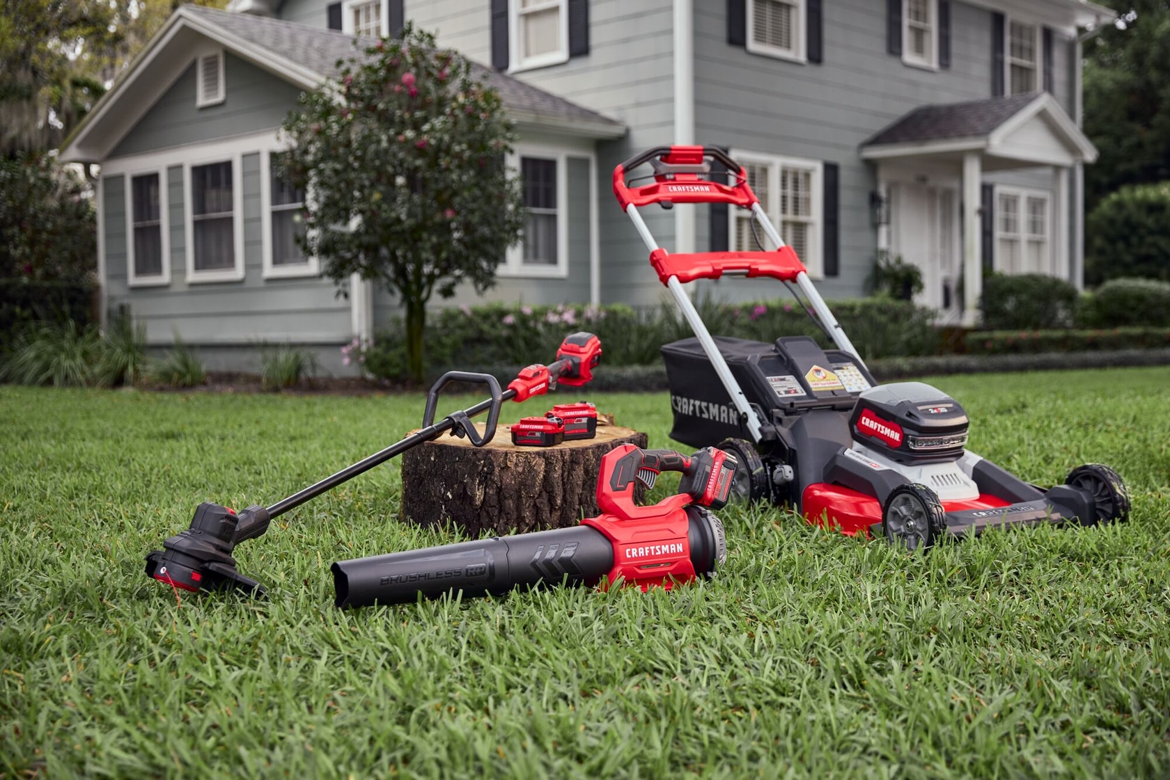 Craftsman lawn tools set CMCB209 with mower, blower, trimmer, and batteries on grass in front of house.