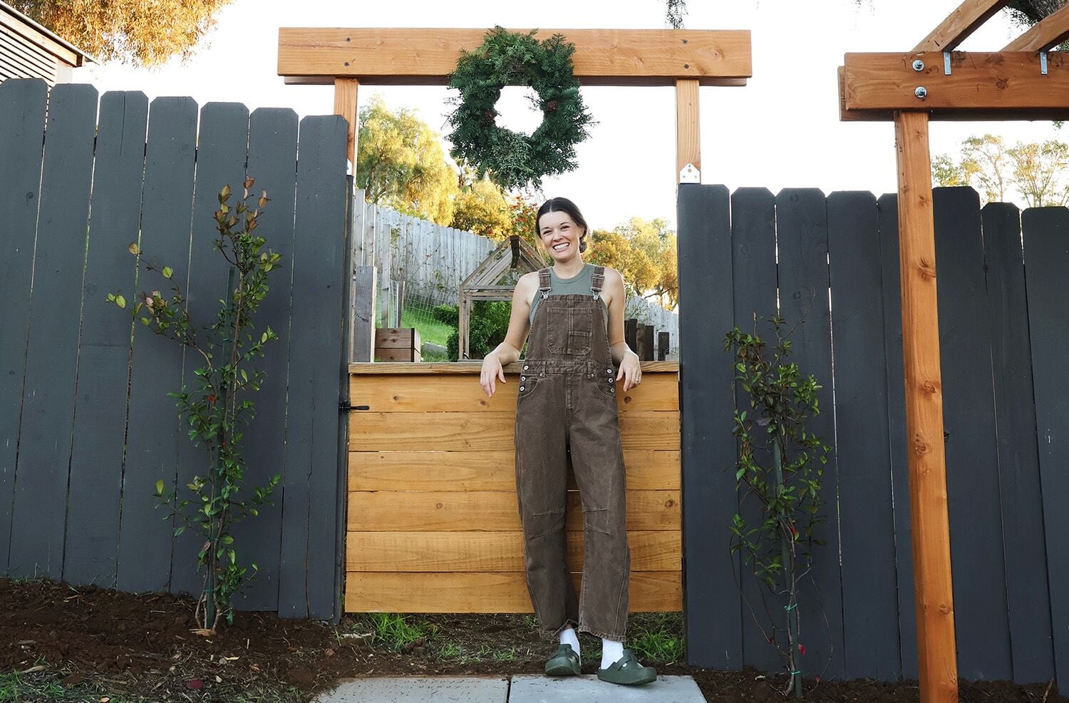 Woman wearing an overall leaning on a wooden fence creating a Trellis