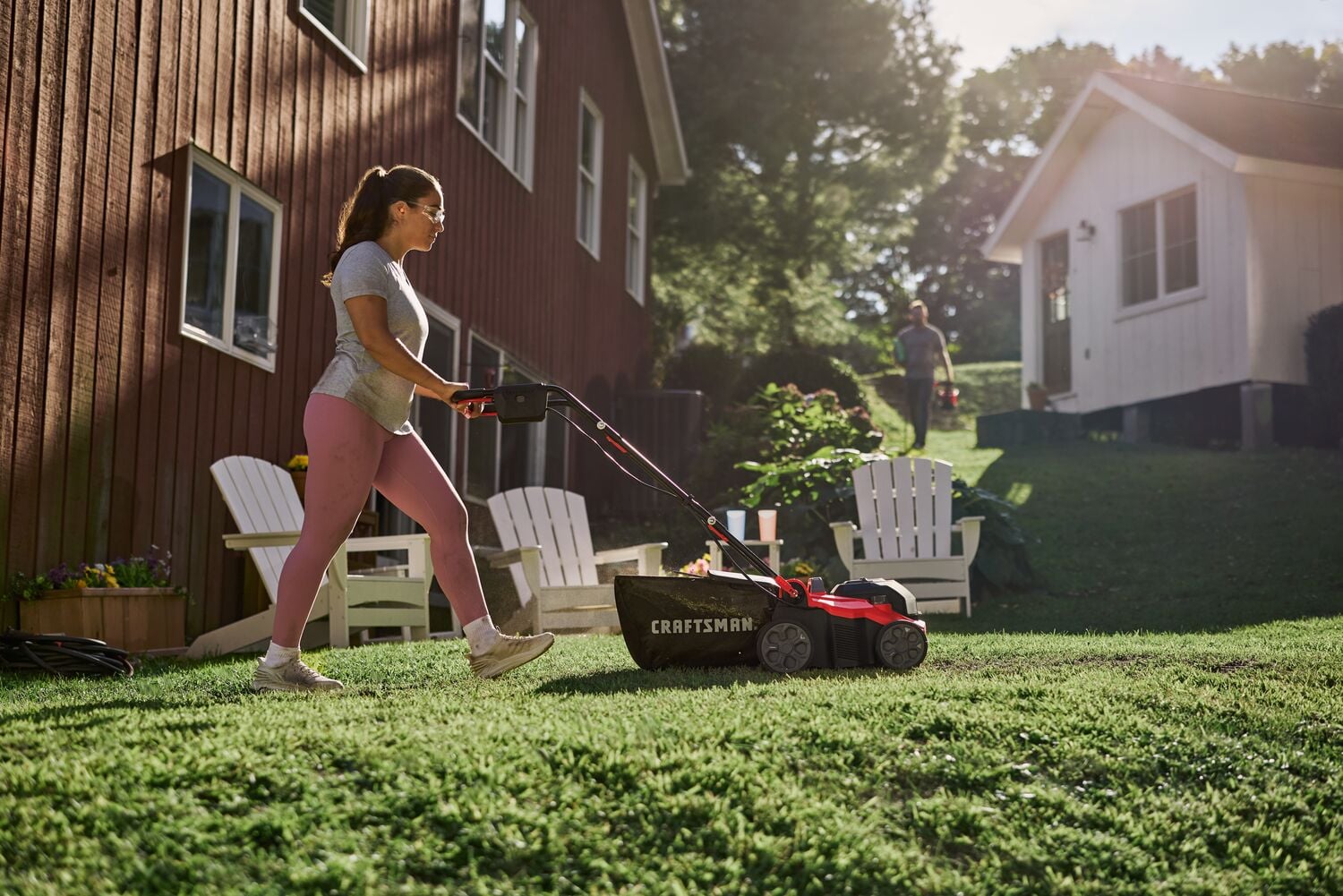 Photo of a Craftsman lawn mower CMCOE210 in use on grass near a house, red and black design, outdoor scene.