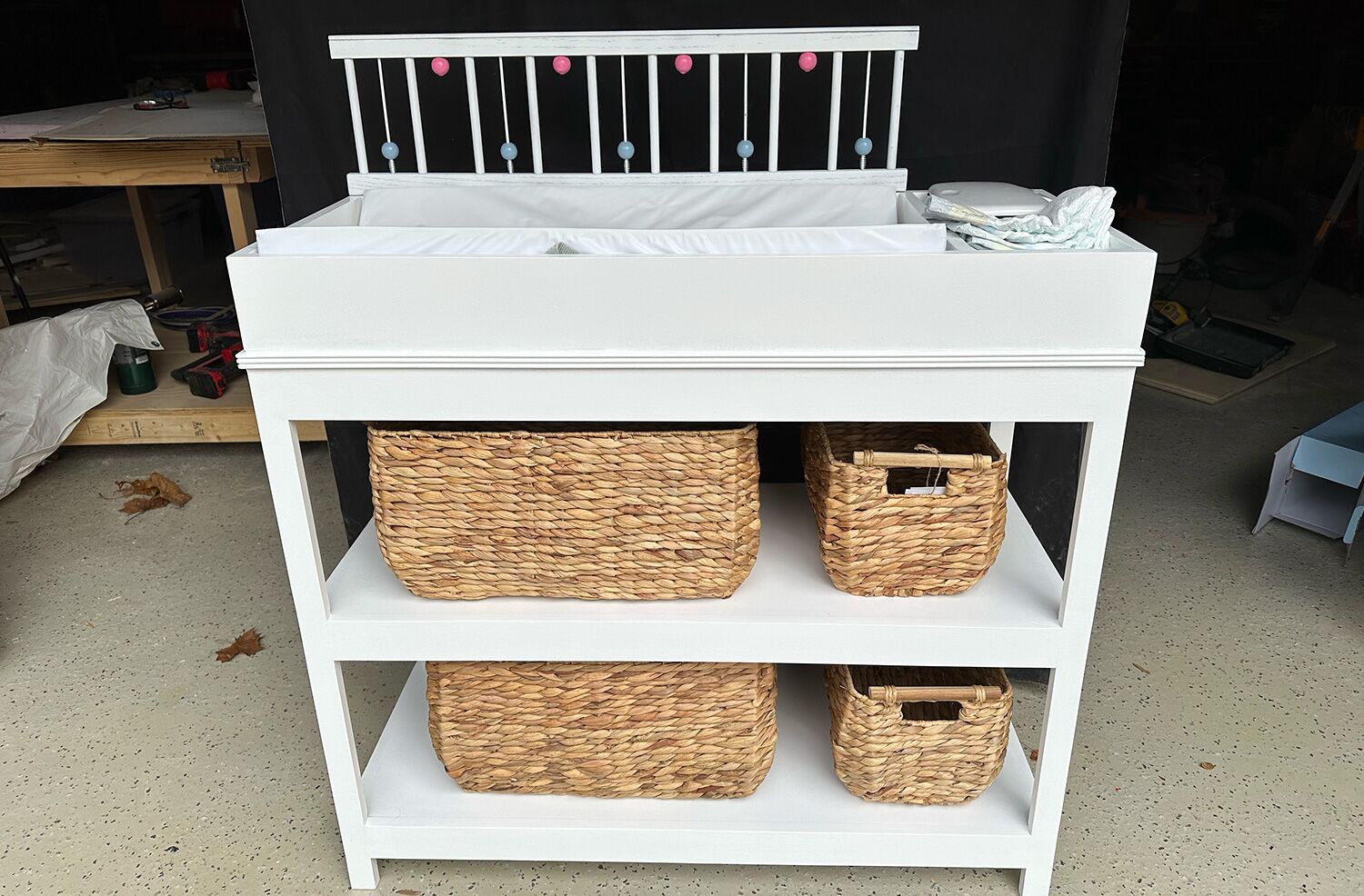 White changing table for babies with brown wooden baskets on the shelves