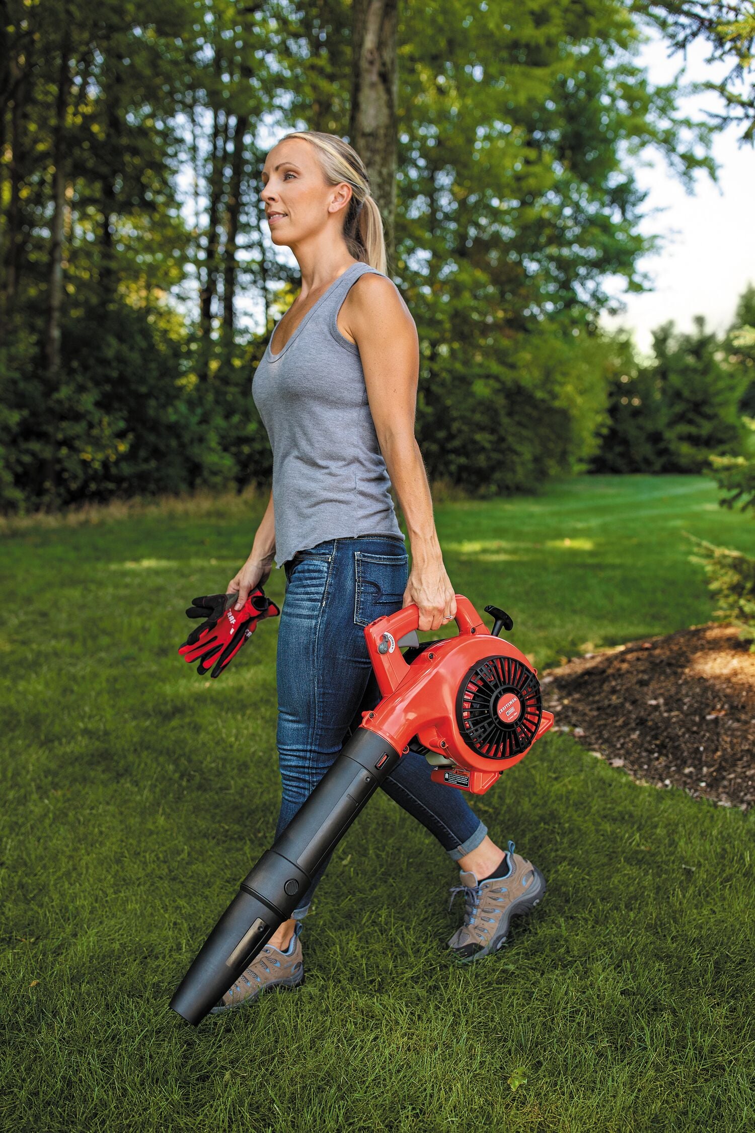 25 C C 2 cycle gas leaf blower being carried by a person outdoors.