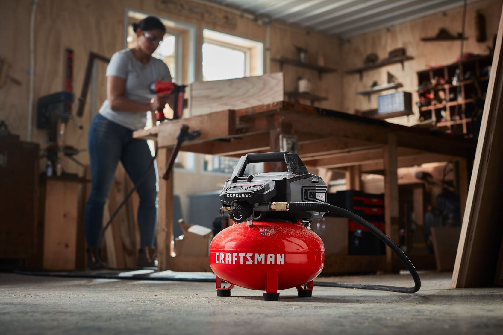 Photo of Craftsman air compressor CMCC2520B on workshop floor, red tank with black top, hose attached, background woodshop.