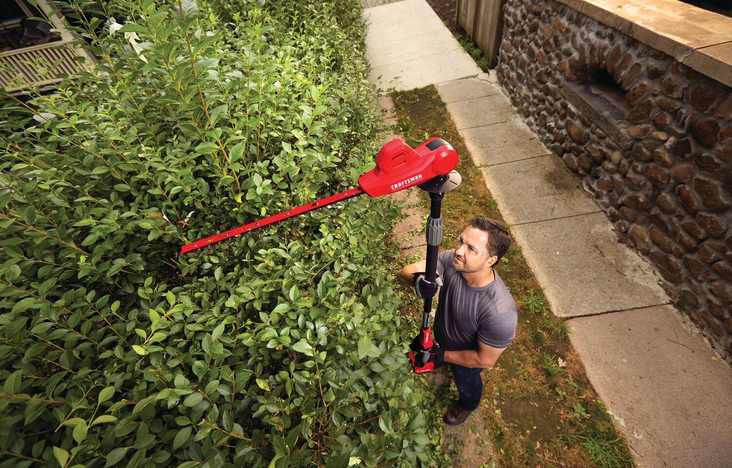 20 volt 18 inch cordless pole hedge trimmer kit being used by a person to trim plants.