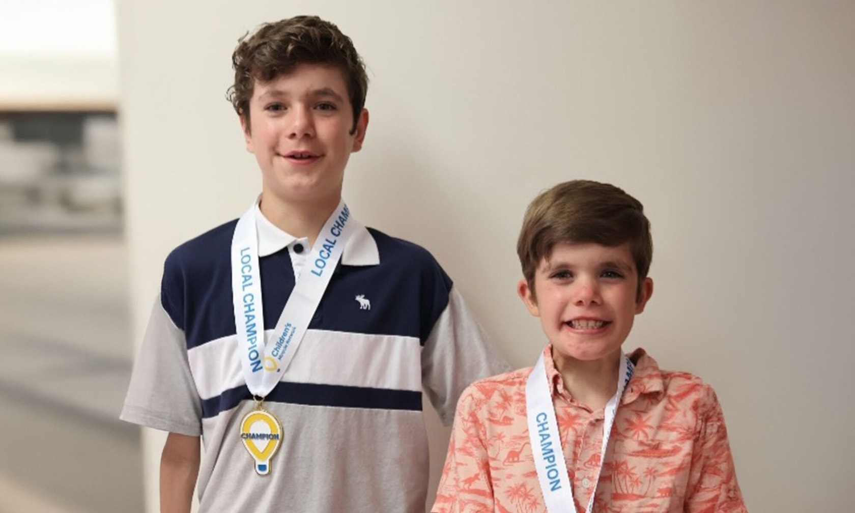 Two children standing side by side, each wearing a lanyard with a medal labeled 'Champion.' Their faces are blurred for privacy.