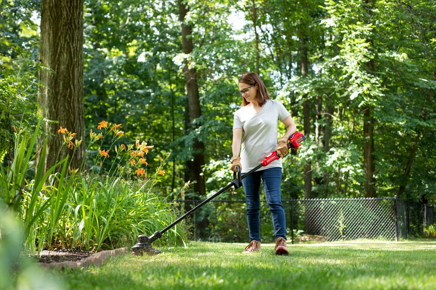 Photo of person using Craftsman string trimmer CMCST930P1 to edge grass near flowerbed outdoors.