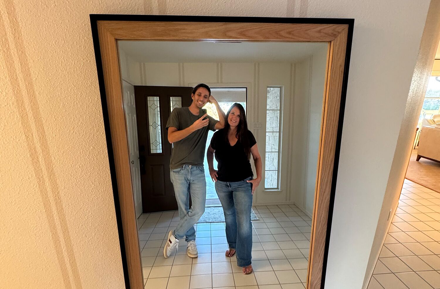A couple takinga picture in a full length mirror with wooden edges