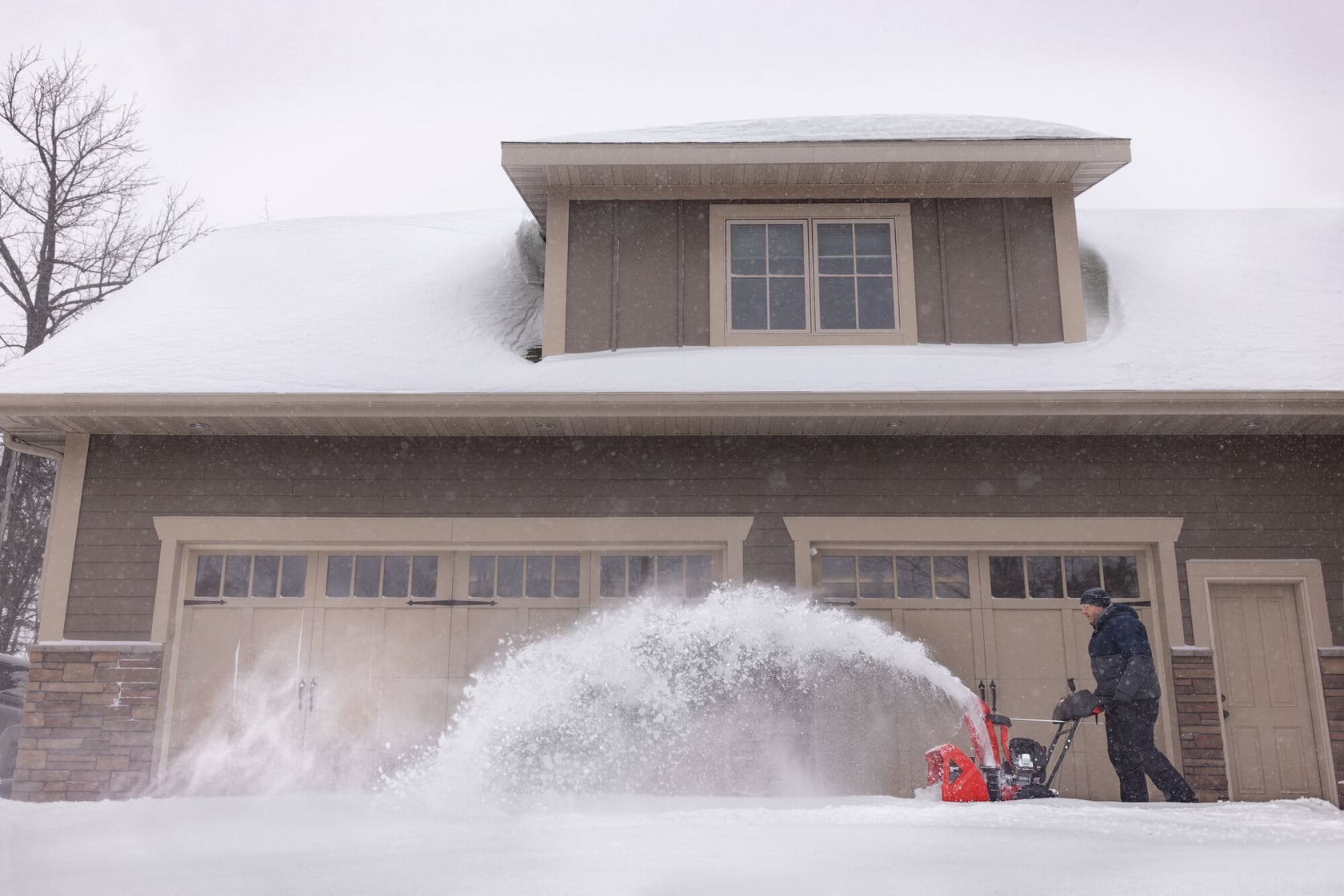 Photo of Craftsman snow blower SKU CMXGBAM213101 clearing snow in front of a house during winter.