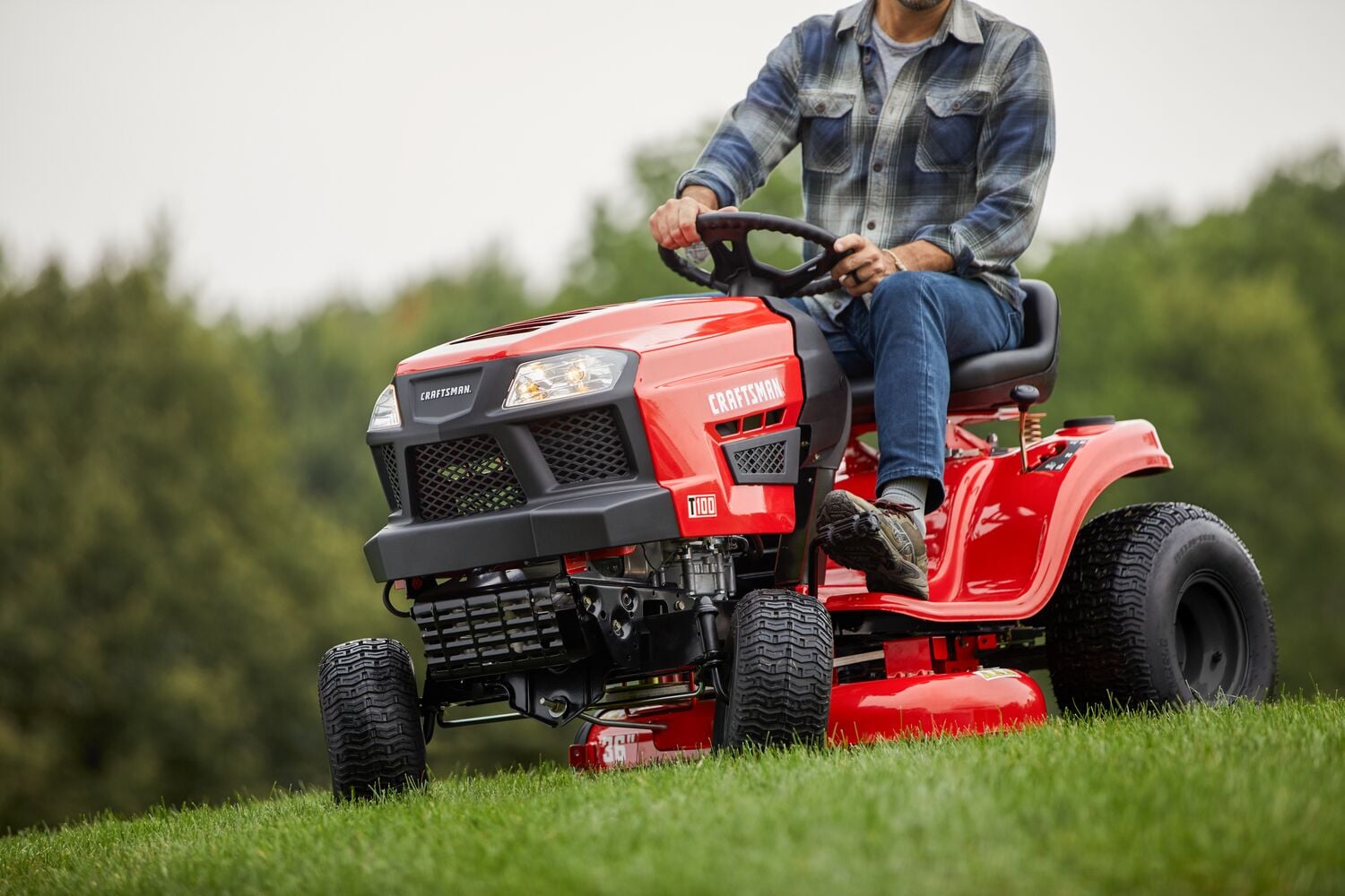 CRAFTSMAN T100 36 In. 11.5 Hp* Gear Drive Riding Mower mowing grass wearing jeans and plaid shirt