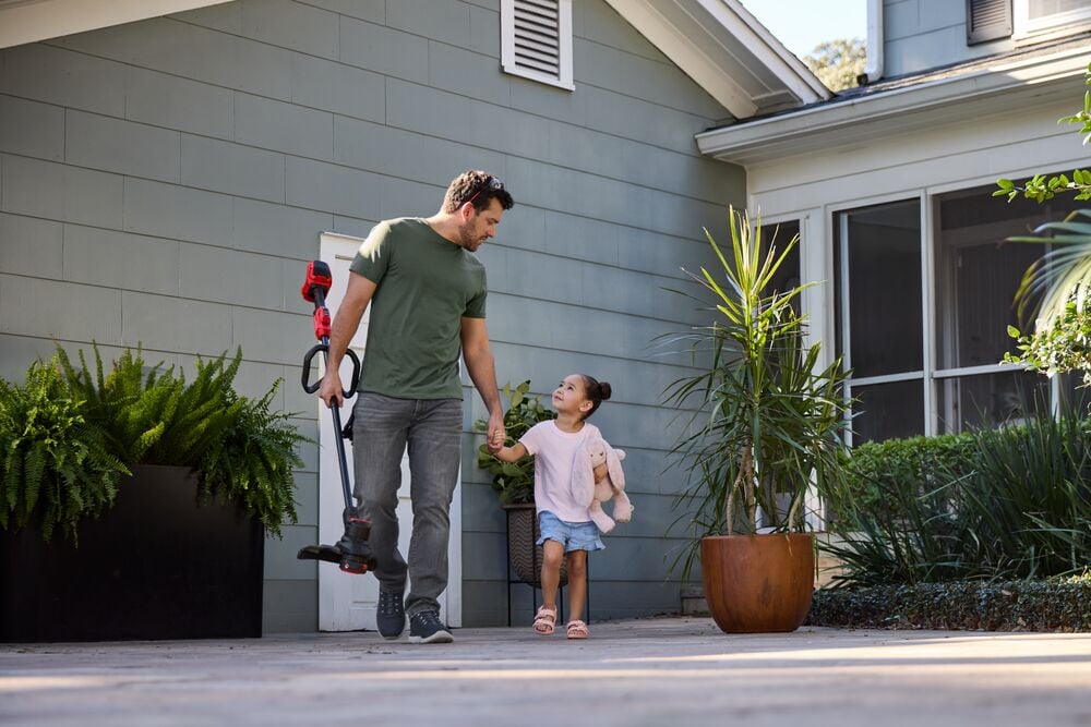 Photo of Craftsman CMCST930P1 string trimmer carried outdoors near a house with plants.