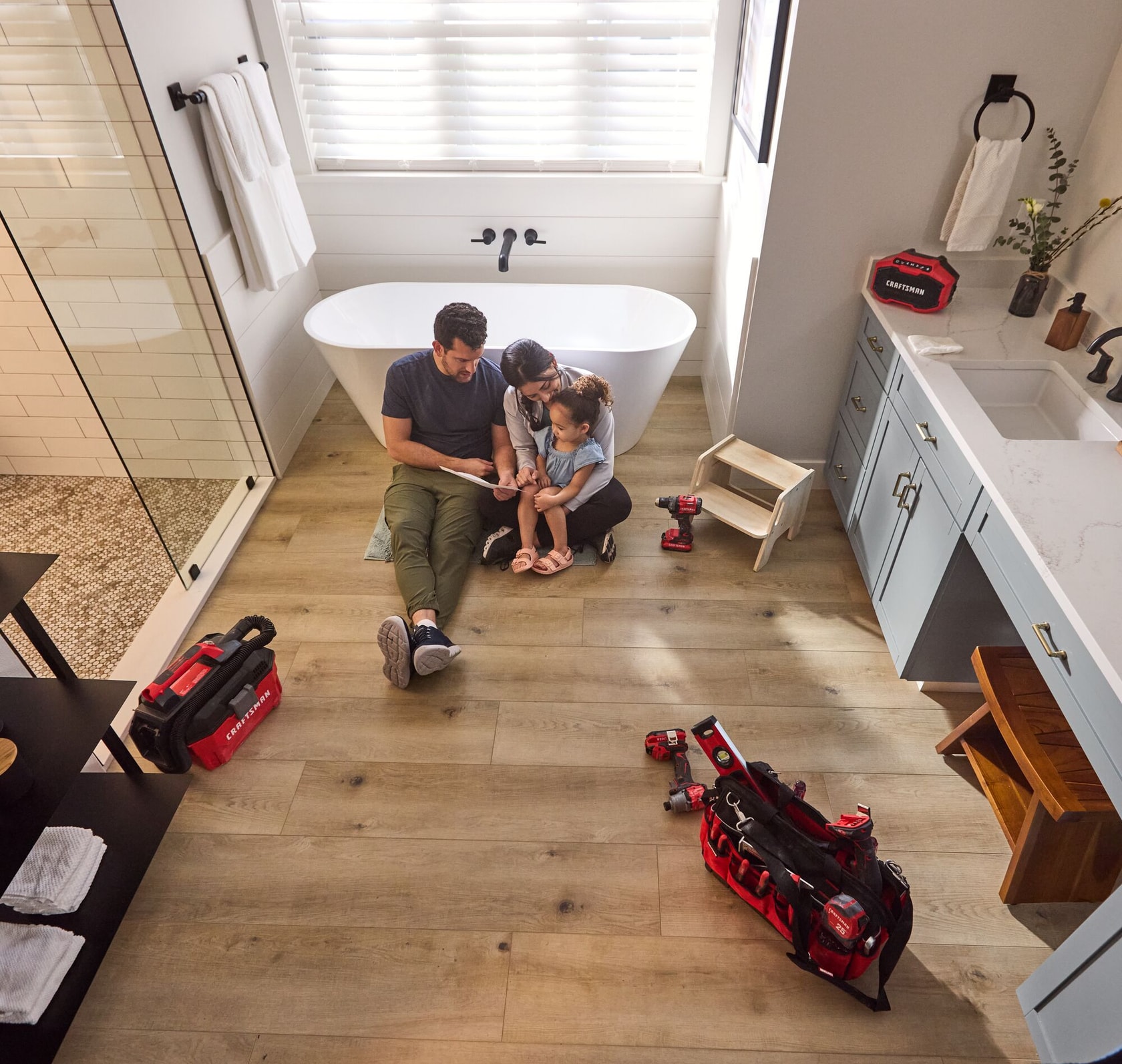 Parents with young daughter in newly renovated bathroom, looking at her drawing of a treehouse