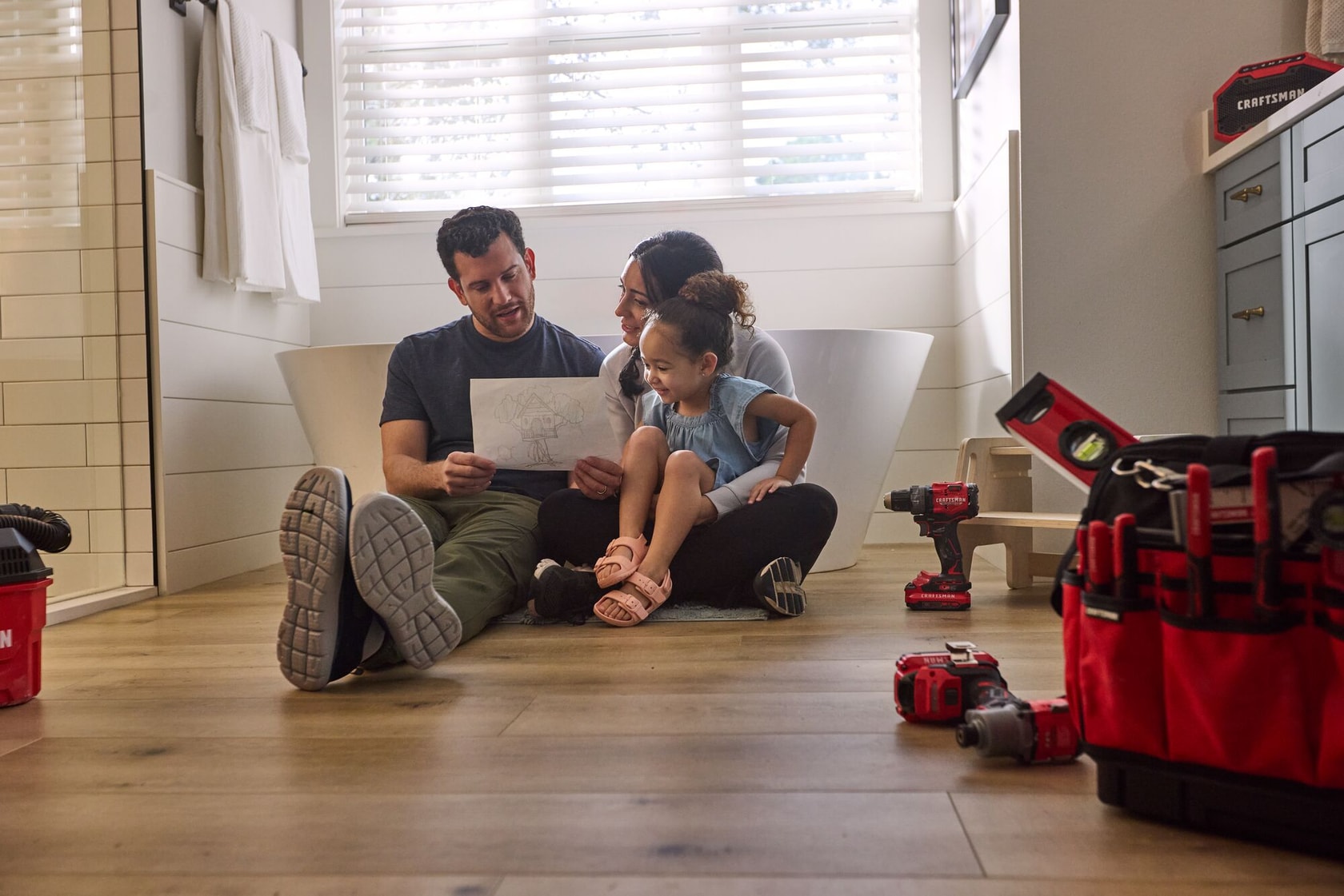 Parents with young daughter in newly renovated bathroom, looking at her drawing of a treehouse
