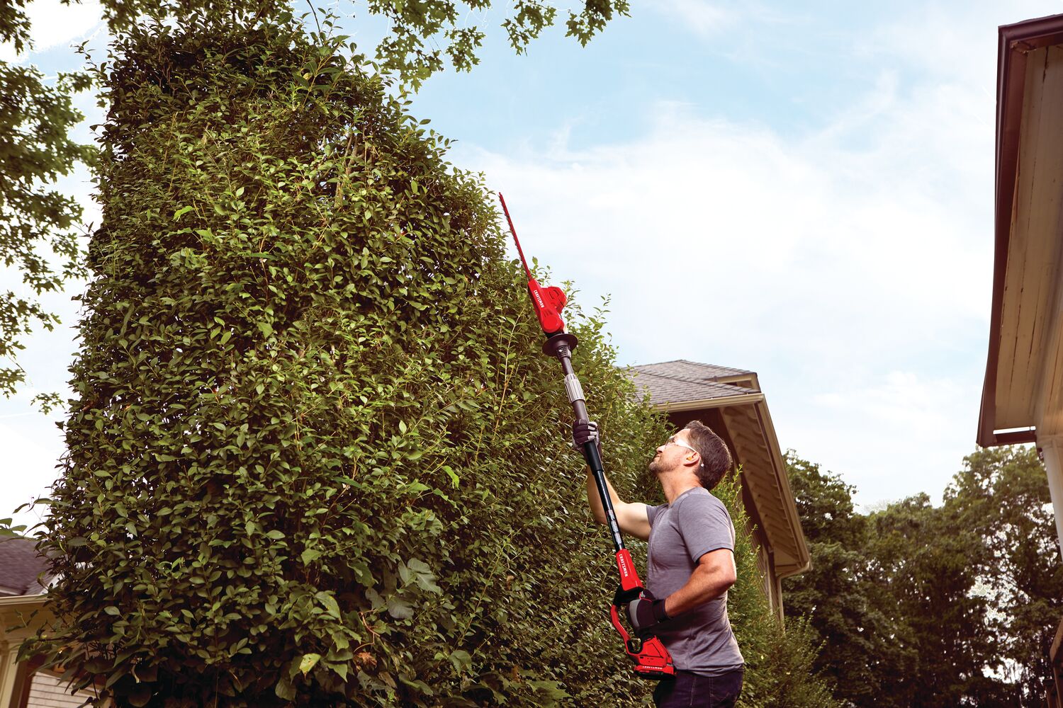 20 volt 18 inch cordless pole hedge trimmer kit being used by a person to trim plants outdoors.