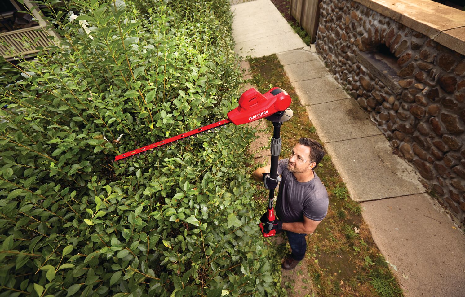 20 volt 18 inch cordless pole hedge trimmer kit being used by a person to trim plants.